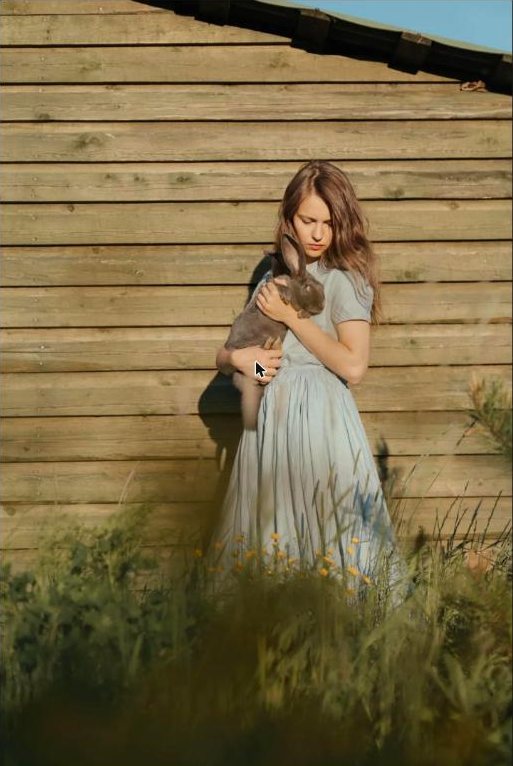 Woman in a long dress holding a rabbit against a wooden barn wall