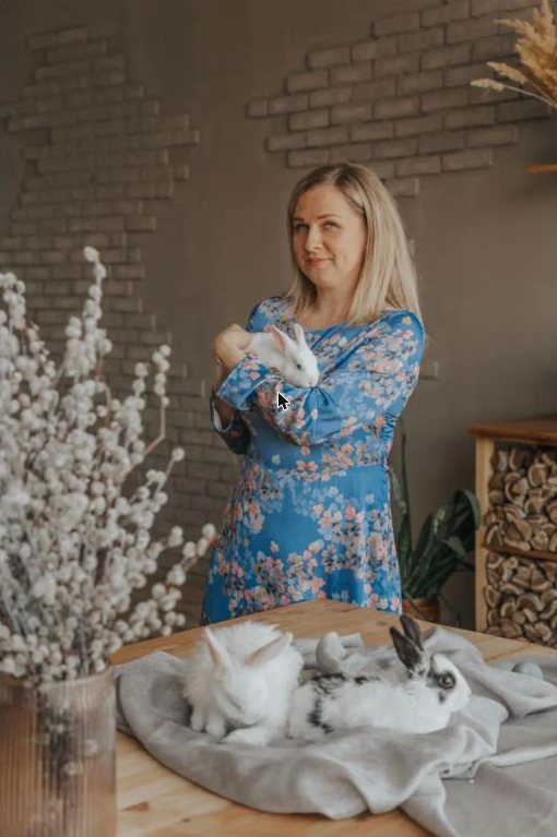 Woman in a blue floral dress holding a white rabbit beside two rabbits on a table